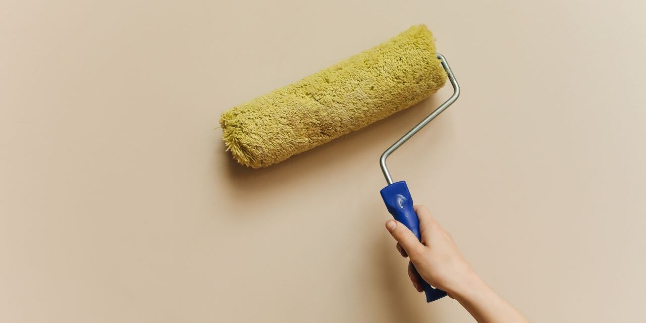 A hand using a yellow paint roller to paint a beige wall. Perfect for DIY and home improvement themes.