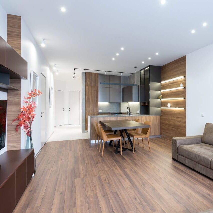Interior of contemporary light decorated apartment with TV set placed against couch in modern apartment with table and kitchen counter